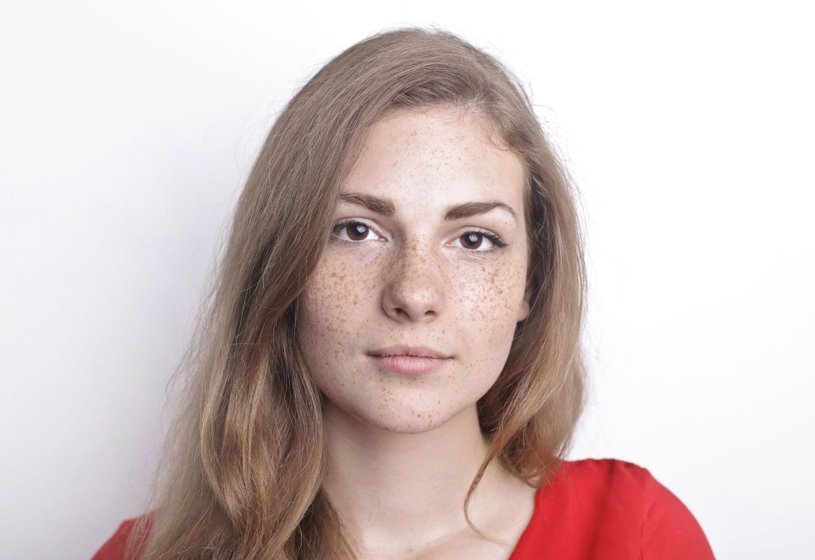 Portrait of a young woman with freckles against a white wall, as the camera sees her